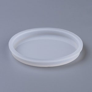 Puede incluir: Un molde de silicona blanco para manualidades de resina. El molde es redondo y tiene un borde elevado.