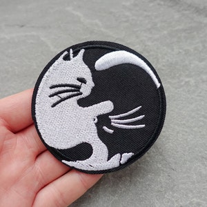 May include: White and black embroidered patch of two cats facing each other in a yin yang design.