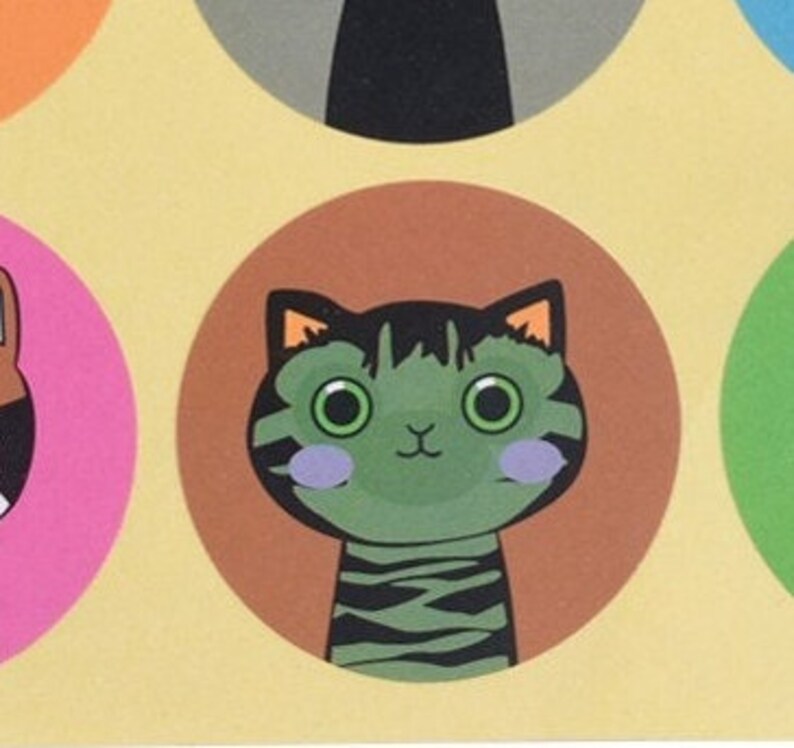 May include: A green and black striped cat with large, round eyes and pink cheeks. The cat is looking directly at the viewer. The cat is on a brown circle with a yellow background.