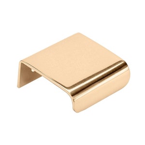 May include: A brushed gold cabinet pull with a rectangular shape and rounded edges.