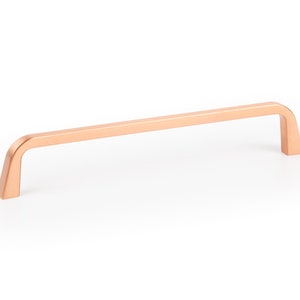 May include: A copper cabinet pull with a rectangular shape and rounded edges. The pull is approximately 10 inches long.