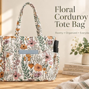 Puede incluir: Un bolso tote de pana blanca con un estampado floral colorido que presenta ilustraciones botánicas en naranja, rosa y verde. El bolso incluye dos asas superiores, bolsillos laterales y un bolsillo frontal con un objeto rectangular azul claro.