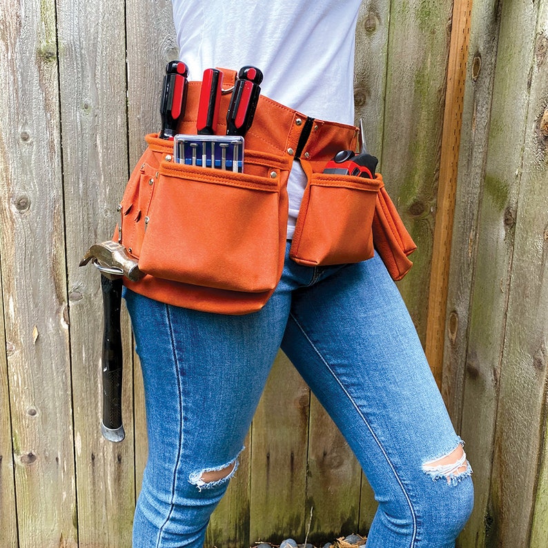 May include: A person wearing a brown leather tool belt with multiple pockets. The belt is filled with tools, including a hammer, screwdrivers, and a measuring tape. The person is wearing blue jeans and a white shirt.