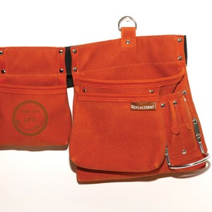 May include: Orange canvas tool belt with multiple pockets and a metal loop. The belt has a black strap and metal rivets. The belt has a label that says "ReplaceMint" and a circular label that says "Sass Joy Life ReplaceMint".