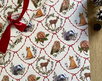 May include: A white wrapping paper with a repeating pattern of woodland animals, including owls, deer, foxes, badgers, and squirrels. The animals are surrounded by red ribbon and holly berries.