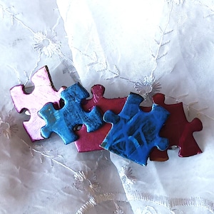 May include: A collection of colorful puzzle pieces in pink, blue, and red. The pieces are arranged together, suggesting a completed puzzle. The background is a white, textured fabric.
