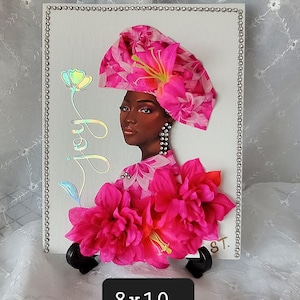 May include: A pink and white floral canvas painting of a woman wearing a pink head wrap with a flower on top. The painting is on a white canvas with a silver border and is on a black easel. The painting is 8x10 inches.