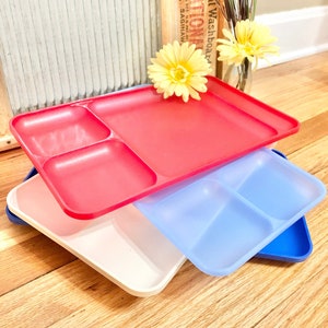 May include: A stack of four divided plates in red, blue, white, and blue. The plates are made of plastic and have a smooth surface. The plates are stacked on a wooden surface.