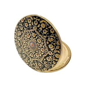 May include: A gold compact with a black enamel lid featuring a detailed floral design in gold and multi-colored accents.