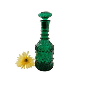 May include: A dark green glass decanter with a decorative design and a matching stopper. The decanter has a round body and a tall, slender neck.