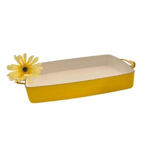 May include: A rectangular yellow baking dish with a white interior and gold-colored handles. A yellow daisy is placed on the side of the dish. The dish is designed for baking and cooking.