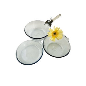May include: Three clear glass baking dishes with blue rims. The dishes are nested together. A yellow flower is sitting on top of the dishes.