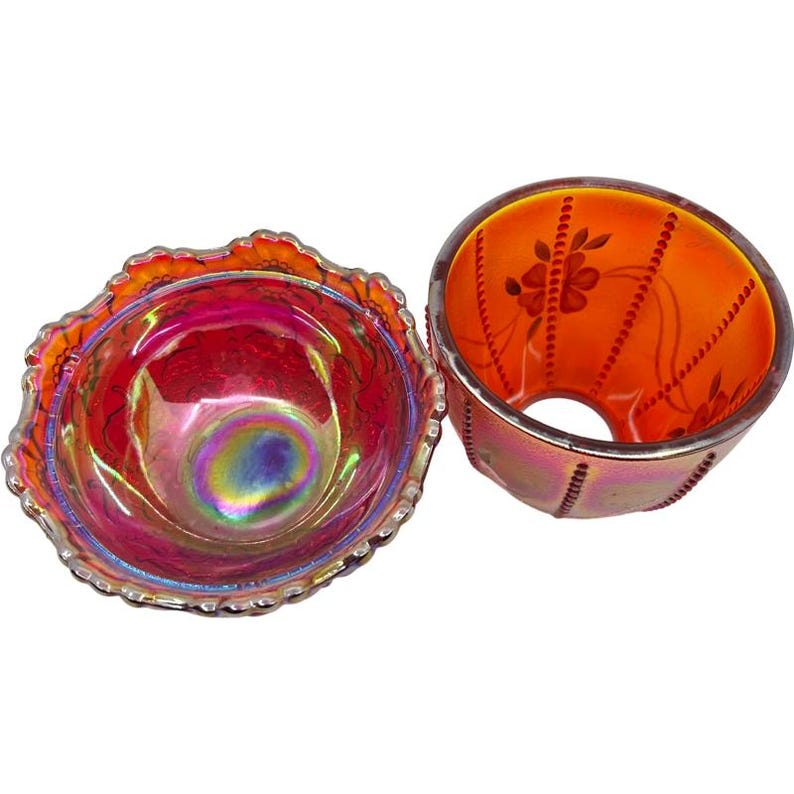 May include: Two iridescent glass bowls. One is a small, round bowl with a ruffled edge. The other is a cylindrical bowl with a floral design and a silver rim. The bowls have a vibrant, colorful appearance with shades of red, orange, and purple.