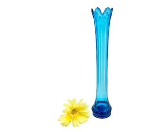 May include: A tall, slender, blue glass vase with a ruffled top. The vase is empty and has a slight curve at the bottom.