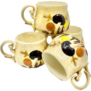 May include: Set of four ceramic coffee mugs with a mushroom and leaf design. The mugs are beige with brown, orange, and yellow accents.