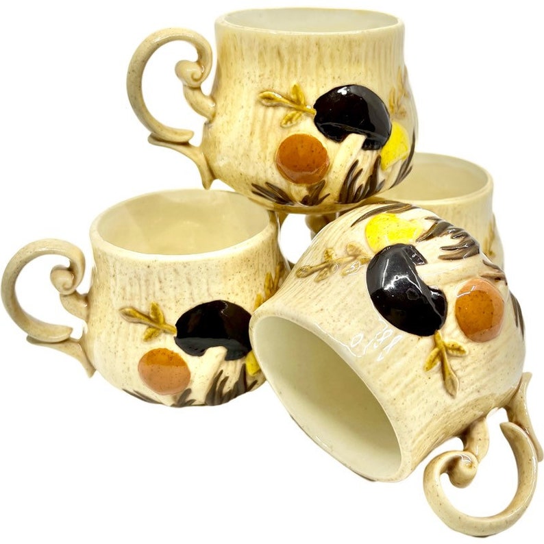 May include: Set of four ceramic coffee mugs with a mushroom and leaf design. The mugs are beige with brown, orange, and yellow accents.