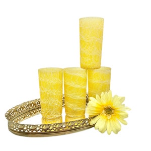 May include: Four yellow glass tumblers with a white crackle design, stacked on a gold oval tray with a floral design. A yellow daisy sits on the tray.