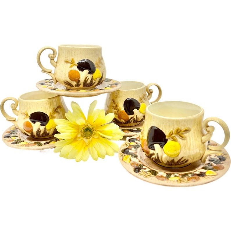 May include: Set of four vintage ceramic teacups and saucers with a mushroom design. The cups and saucers are beige with brown, yellow, and orange accents.