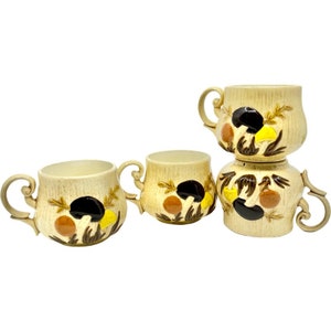 May include: Set of four ceramic mugs with a mushroom design. The mugs are beige with brown, black, orange, and yellow accents.