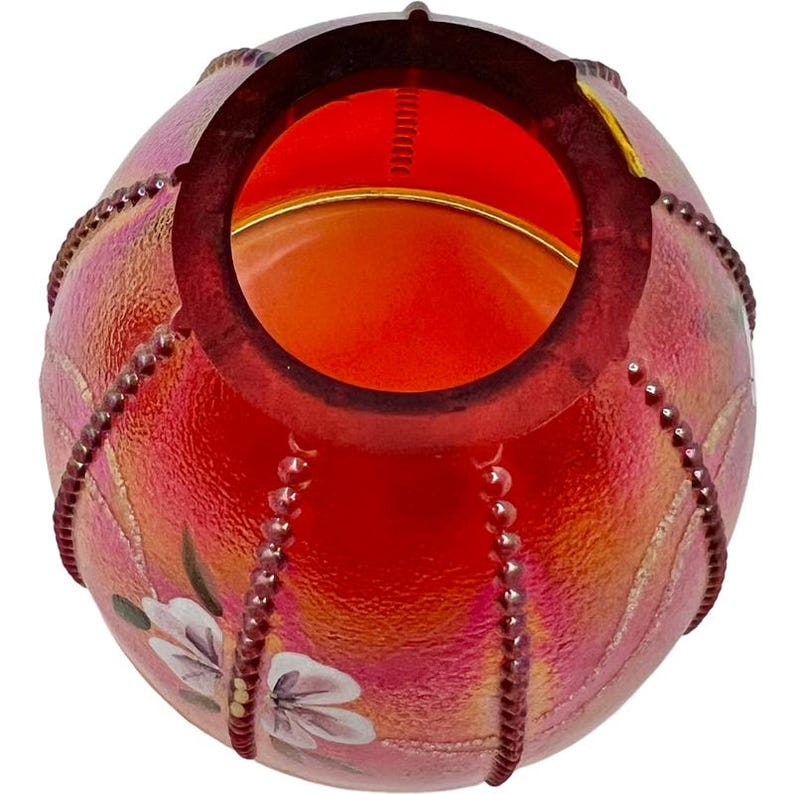 May include: A red iridescent glass bowl with a round opening. The bowl has a floral design and is decorated with beaded accents. The interior is a bright orange color.