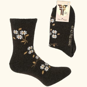 May include: Dark brown wool socks with a floral pattern. The socks feature white and gold flowers and leaves. The tag reads "Wool 100%" and "Made in Mongolia". The size is 40-42.