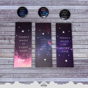 以下が含まれることがあります： 銀河をテーマにしたブックマーク3つ。ブックマークには「There's magic in every page」というテキストが印刷されています。ブックマークは木製の背景の上に置かれています。