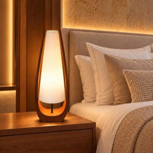Könnte beinhalten: Eine Tischleuchte mit einem hohen, konischen weißen Lampenschirm, der in einem geschwungenen Rahmen aus dunklem Holz hängt. Die Lampe strahlt ein warmes, sanftes Licht aus und wird von einem schwarzen Mittelstab an der Holzbasis gehalten.