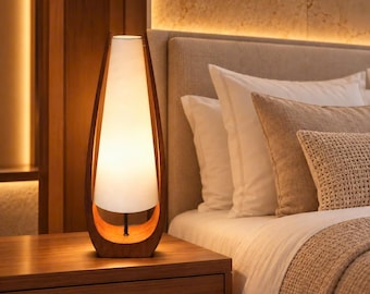May include: A table lamp featuring a tall, conical white lampshade suspended within a curved, dark wood frame. The lamp emits a warm, soft glow, with the shade supported by a central black stem attached to the base of the wooden structure.