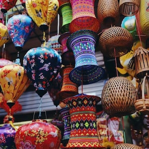 May include: A collection of colorful, hanging lanterns in various shapes and sizes. The lanterns feature floral, geometric, and bird patterns in shades of red, blue, yellow, and green. Some are made of woven materials, while others are silk.
