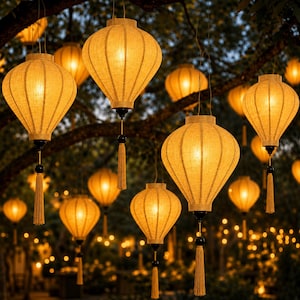 Może przedstawiać: Kilka podświetlonych, żółtych papierowych lampionów o różnych rozmiarach wisi na gałęziach drzew. Każdy lampion ma czarną podstawę, frędzel i ciepłą poświatę. Tło jest rozmyte, co sugeruje otoczenie zewnętrzne.