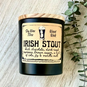 Op de afbeelding: Een zwarte kaars pot met een houten deksel. Het etiket luidt "Soy Wax 10oz Wood Wick Irish Stout Rich chocolate, dark roast, espresso, brown sugar, a hint of cola, fig & vanilla malt www.deconstructedcandles.com"