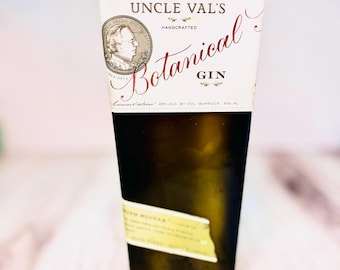 May include: A dark green rectangular bottle of Uncle Val's Botanical Gin. The label features a portrait, the words "Uncle Val's Handcrafted Botanical Gin", and other text. The bottle is on a light wood surface.