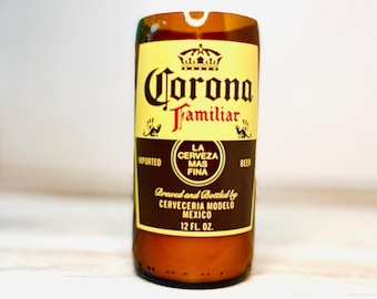 May include: A brown glass bottle with the "Corona Familiar" label. The label is yellow and brown with the text "IMPORTED", "LA CERVEZA MAS FINA", and "12 FL. OZ.". The bottle is cut at the top.