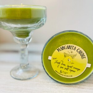 May include: A green margarita candle in a glass jar with a yellow label that reads "Margarita Candle" and "Fresh lime, sweet orange & sea salt agave".