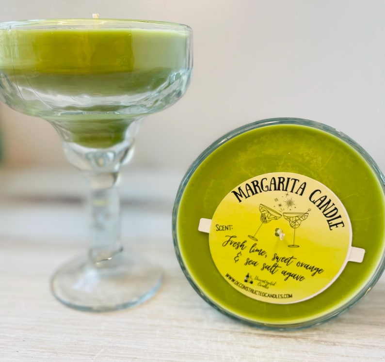 May include: A green margarita candle in a glass jar with a yellow label that reads "Margarita Candle" and "Fresh lime, sweet orange & sea salt agave".