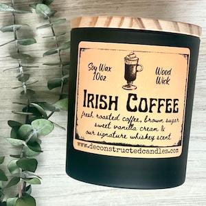 May include: A black candle jar with a wooden lid. The label reads "Soy Wax 10oz" and "Wood Wick". The candle is labeled "Irish Coffee" and describes the scent as "fresh roasted coffee, brown sugar, sweet vanilla cream & our signature whiskey scent". The website address "www.deconstructedcandles.com" is printed on the label.