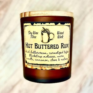 May include: A brown glass candle jar with a wooden lid. The label reads "Soy Wax 10oz Wood Wick HOT BUTTERED RUM Rich buttercream, carmelized toffee blackstrap molasses, warm vanilla, cinnamon, clove & nutmeg www.deconstructedcandles.com"