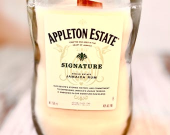 May include: A white candle in a clear glass bottle with a brown wooden lid. The bottle has a label that reads "Appleton Estate Signature Single Estate Jamaica Rum". The label also includes the text "Our estate's storied history, and commitment to expressing Jamaica's unique terroir, is embodied in our signature rum blend." and "Established 1749 Nassau Valley".