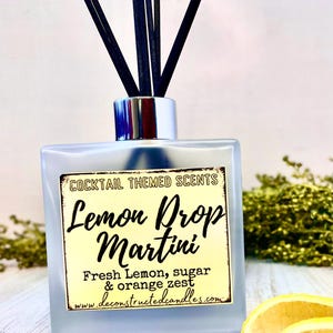 Könnte beinhalten: Ein Diffusor aus klarem Glas mit schwarzen Schilfrohren und einem Etikett mit der Aufschrift "Cocktail Themed Scents Lemon Drop Martini Fresh Lemon, sugar & orange zest www.deconstructedcandles.com".