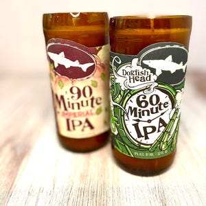 May include: Two repurposed beer bottle glasses. One features a label with a shark and the text "90 Minute Imperial IPA". The other glass has a label with a shark and the text "Dogfish Head 60 Minute IPA". Both glasses are brown.