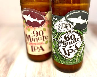 May include: Two repurposed beer bottle glasses. One features a label with a shark and the text "90 Minute Imperial IPA". The other glass has a label with a shark and the text "Dogfish Head 60 Minute IPA". Both glasses are brown.