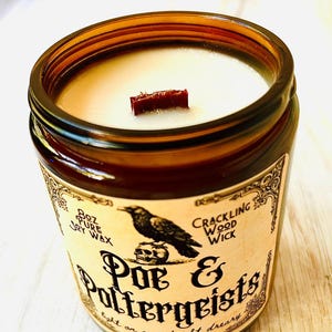 K&ouml;nnte beinhalten: Braune Glas-Kerze mit Holzdocht. Das Etikett zeigt einen schwarzen Raben &uuml;ber einem Totenkopf mit den Worten "Poe & Poltergeists". Die Kerze enth&auml;lt 227g reines Sojawachs und einen knisternden Holzdocht.