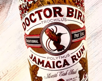 May include: A brown glass bottle with a white label featuring a red hummingbird and the text "Doctor Bird Traditional Pot Still Jamaica Rum Moscatel Cask Finish 100 Proof 50% Alc. By Vol."