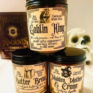K&ouml;nnte beinhalten: Drei Sojawachskerzen in Gl&auml;sern mit schwarzen Deckeln. Die Etiketten zeigen Illustrationen und Text, darunter "Goblin King", "Butter Brew" und "Maiden, Mother & Crone". Jede Kerze ist 227g und hat einen knisternden Holzdocht.