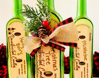 May include: Three green glass bottles repurposed as candles, each with a cork stopper. The central bottle features a wooden tag with "Christmas Tree" text, a burlap and plaid bow, pine, and berries. The other bottles have labels with "Holly Berry" and "Mistletoe" text.