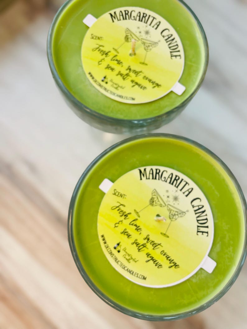 May include: Two green glass margarita candle jars with white labels. The labels have a yellow watercolour background and say "MARGARITA CANDLE" in black script. The labels also say "SCENT: Fresh lime, sweet orange & sea salt agave" in black script.