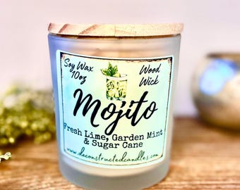 Może przedstawiać: Szklany słoik na świecę z matowym wykończeniem i drewnianą pokrywką. Etykieta zawiera napis "Soy Wax 10oz Wood Wick Mojito Fresh Lime, Garden Mint & Sugar Cane www.deconstructedcandles.com".