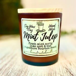 May include: A brown glass candle jar with a wooden lid. The label reads "Mint Julep" with text indicating soy wax, a wood wick, and the scent description. The candle is 283 grams.
