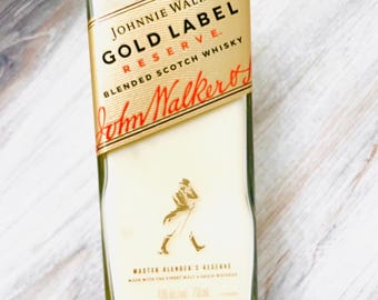 May include: A rectangular glass candle holder with a gold label featuring the text "JOHNNIE WALKER GOLD LABEL RESERVE BLENDED SCOTCH WHISKY". The candle holder has a white wax interior and a logo of a man walking. The candle holder is 750 ml.