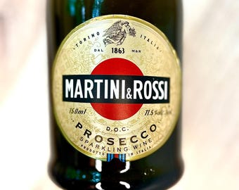 May include: A green glass bottle of Martini & Rossi Prosecco sparkling wine. The label features the brand name, a red circle, and text indicating 150ml and 11.5% alcohol content. The label also includes the text "PROSECCO SPARKLING WINE PRODOTTO IN ITALIA."